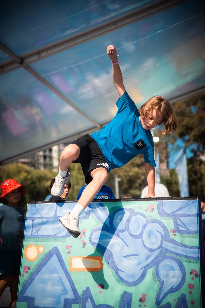 A young traceur leaping over a wall under the Covered Festival marquee