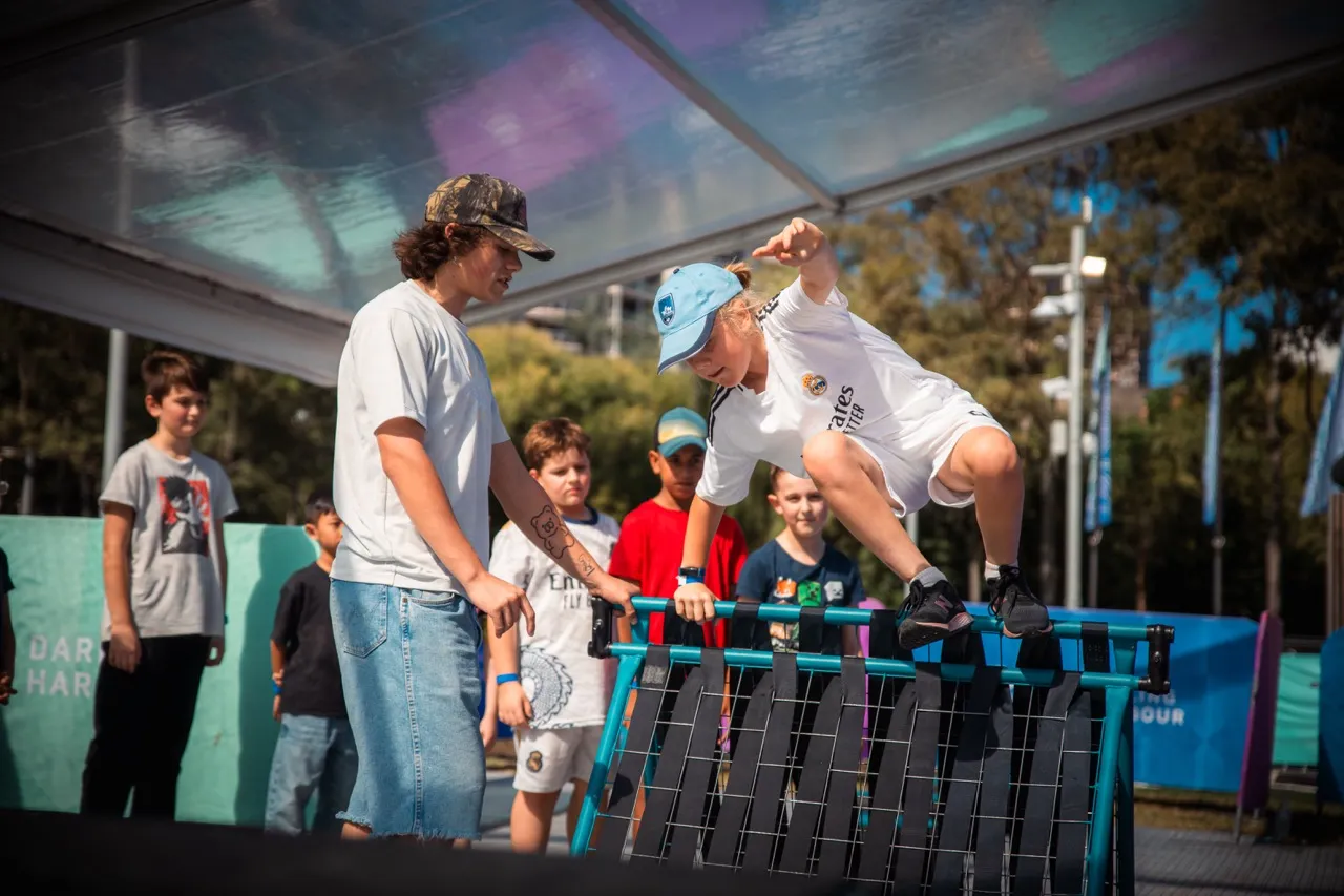 A coach guiding a child over an obstacle under the festival marquee