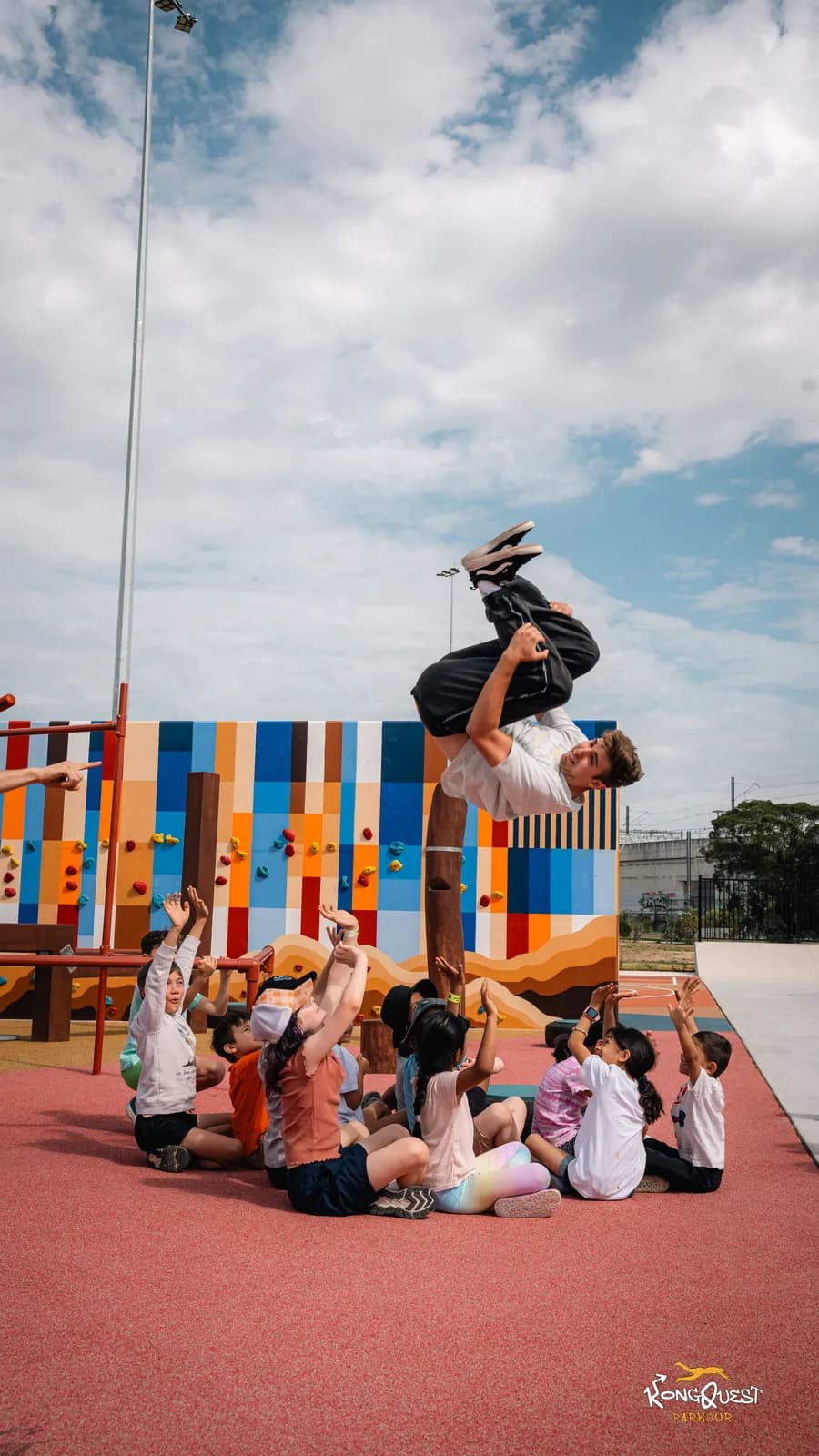 A KongQuest coach holding a handstand while a circle of kids watches in awe